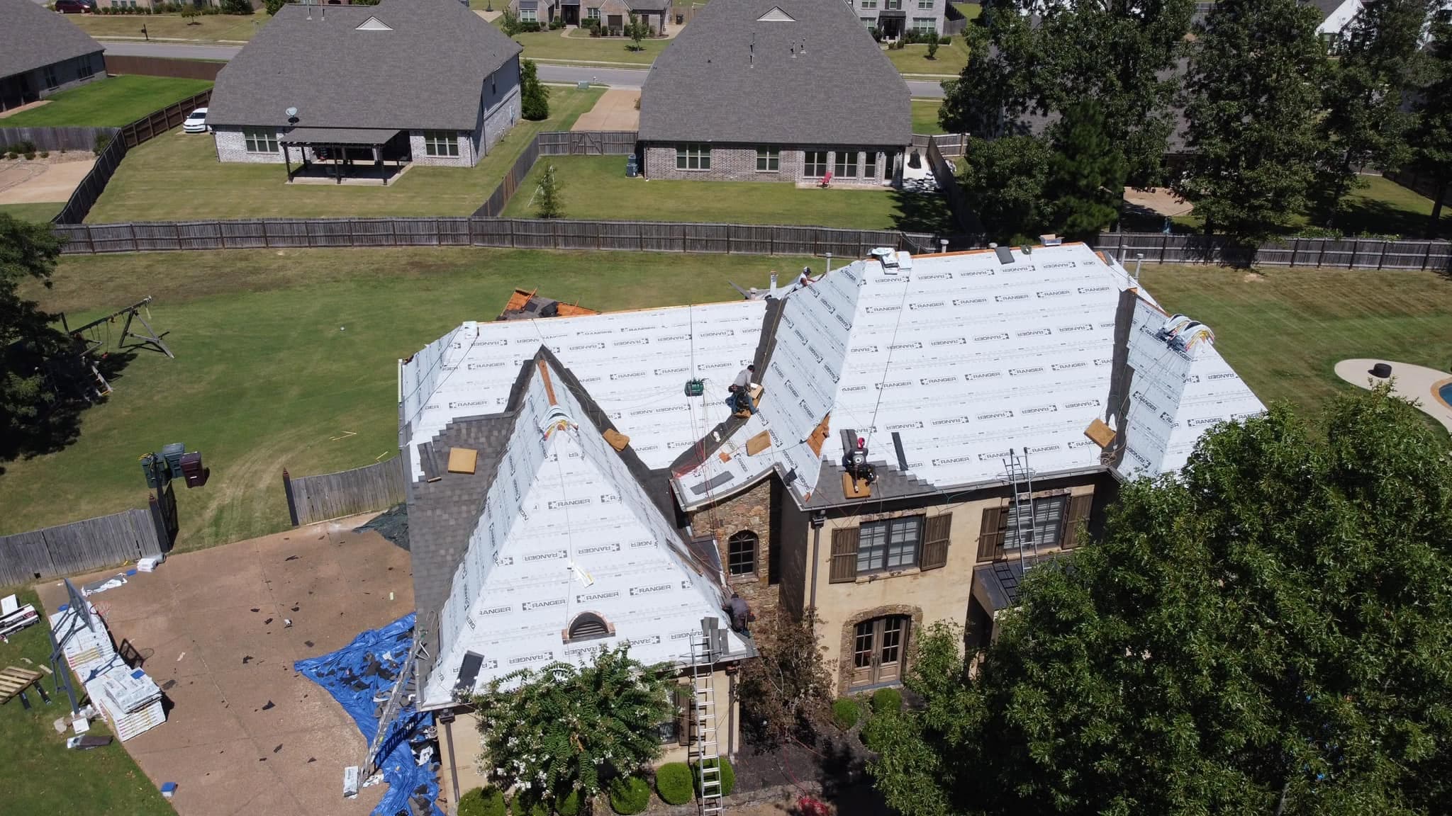 Precision Roofing crew installing synthetic underlayment on a large Mid-South home, drone view